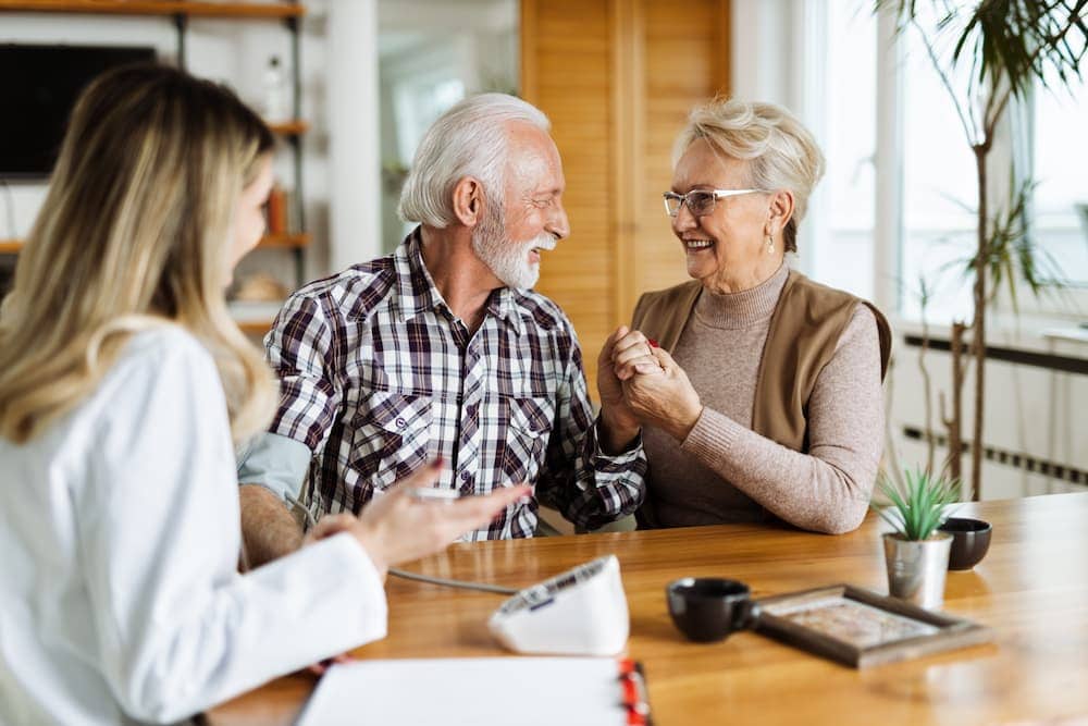 Happy senior couple meeting with a young female healthcare professional or insurance agent to discuss their Medicare coverage options.
